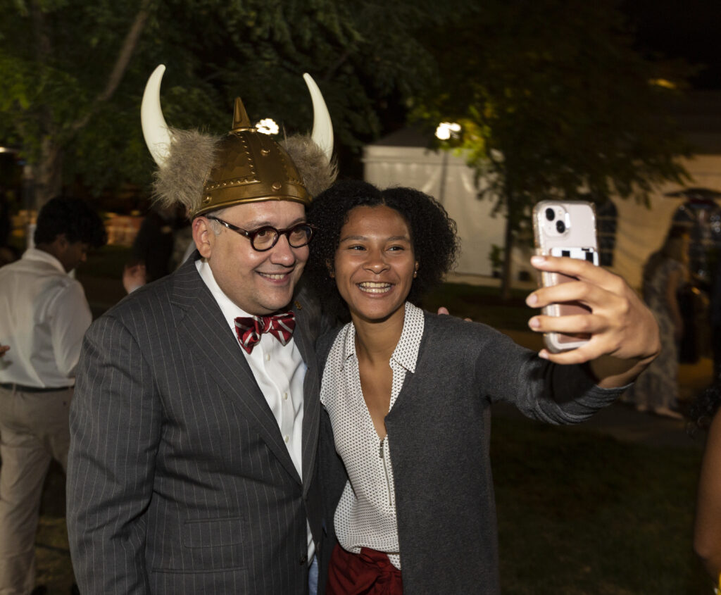 Chancellor Martin posing for a selfie with a student. The chancellor is wearing a photo prop Viking helmet for fun