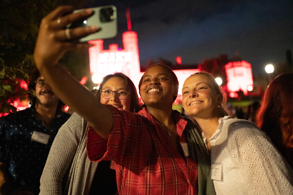 Students taking a selfie in front of red-lit Brookings Hall